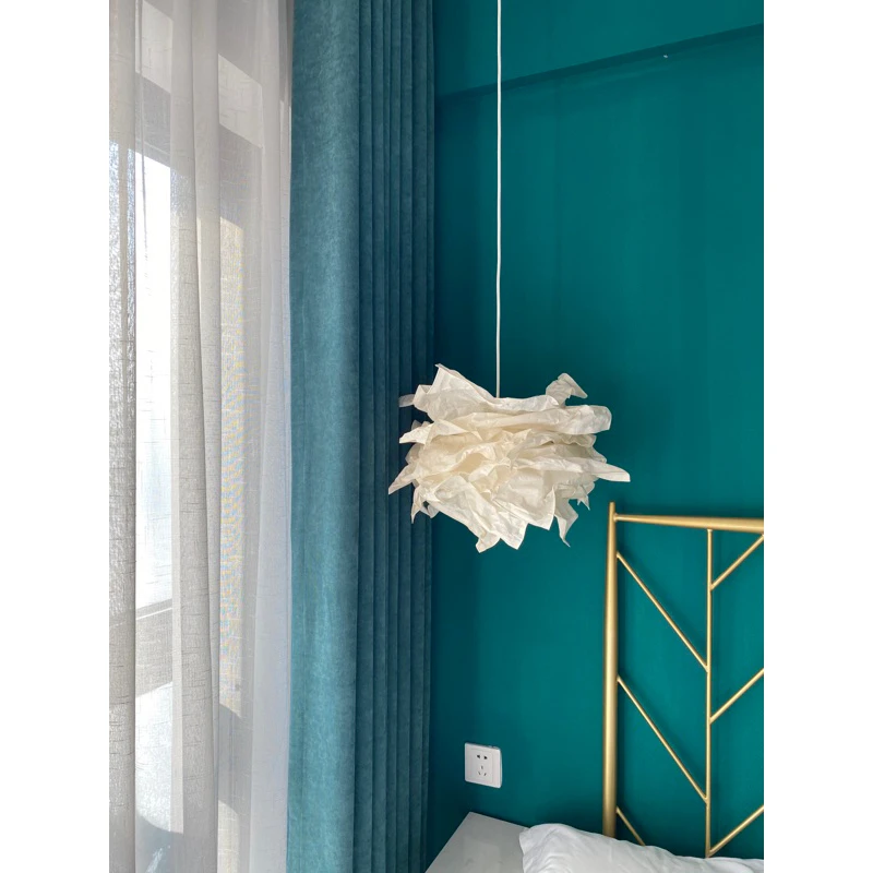 Đèn trần trang trí IKEA SINNERLIG màu trắng, thiết kế dạng hoa giấy, treo trên giường với đầu giường kim loại mạ vàng và tường màu xanh ngọc.
