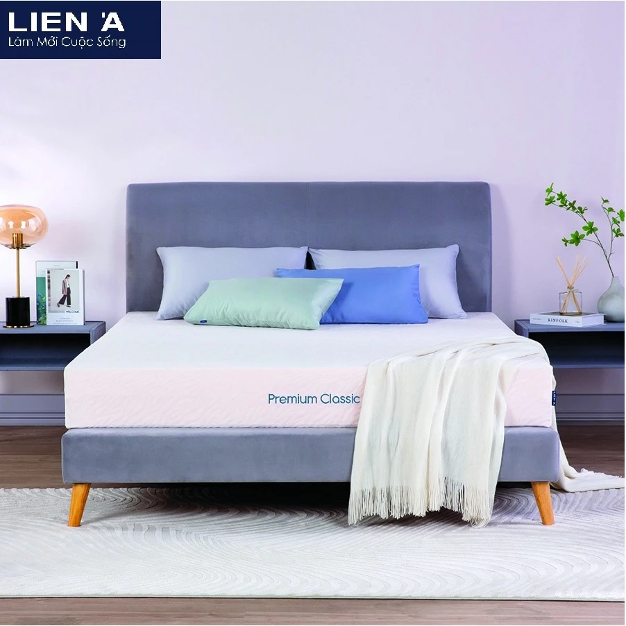 Nệm Liên Á Classic màu trắng, đặt trên giường vải nỉ xám, đi kèm gối và chăn trang trí, tạo nên không gian phòng ngủ tối giản và sang trọng.